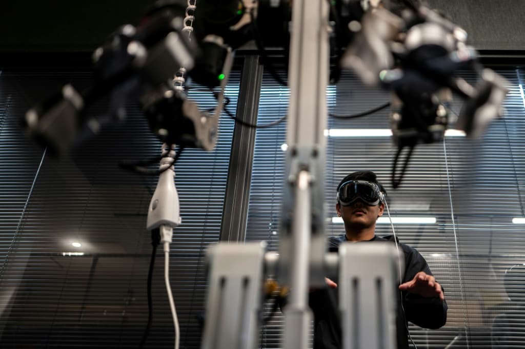 An engineer (back), of company Enactic, tele-operating with a VR headset and a robotic arm in the company's office in Tokyo